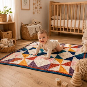 Peut inclure: Une couverture carrée au crochet présentant un motif géométrique de triangles dans des tons crème, bleu marine, jaune moutarde, terre cuite et rose pâle. La couverture possède une bordure bleu foncé et est faite de segments triangulaires.