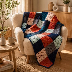 Puede incluir: Una manta de ganchillo compuesta por un mosaico de motivos cuadrados en azul marino, naranja quemado, rosa claro y azul pálido. La manta está colocada sobre un sillón texturizado de color crema, mostrando un patrón de punto calado.