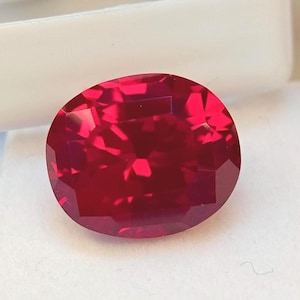 Könnte beinhalten: Ein leuchtender, oval geschliffener Edelstein in einer tiefen, gesättigten roten Farbe. Der Stein hat eine facettierte Oberfläche, die das Licht reflektiert und ein brillantes, funkelndes Aussehen mit geometrischen Mustern erzeugt.