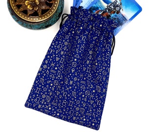 May include: A blue velvet bag with gold zodiac symbols and stars printed on it. The bag is open and has a drawstring closure. Three tarot cards are partially visible inside the bag.