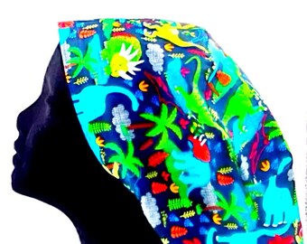Könnte beinhalten: Ein farbenfrohes Kopfbedeckung mit einem Dinosaurier-Muster. Der Stoff ist tiefblau und mit Dinosauriern in Grün- und Türkistönen sowie roten, gelben und weißen Akzenten verziert. Das Design umfasst Palmen und Wolken.