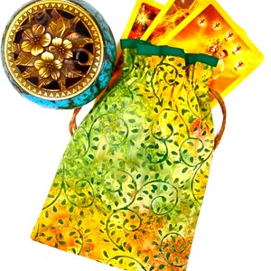 May include: A yellow and green drawstring bag with a floral pattern. The bag is filled with tarot cards. A small blue and gold incense burner is in the background.