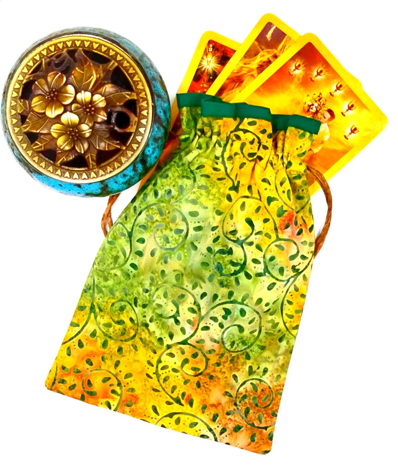 May include: A yellow and green drawstring bag with a floral pattern. The bag is filled with tarot cards. A small blue and gold incense burner is in the background.