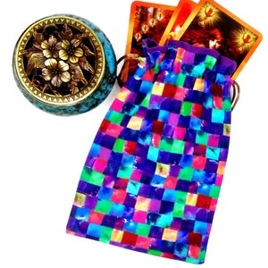 May include: A colorful patchwork drawstring bag with a teal and brass incense burner. The bag is filled with tarot cards with images of a woman and a chalice.