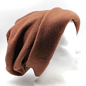 May include: A solid brown beanie made of a soft, textured fleece fabric. The hat features a wide, folded cuff at the base and a slouchy, relaxed fit that gathers at the back, providing a simple and functional head covering design.