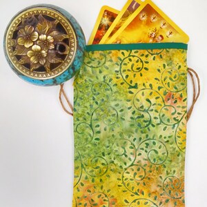 May include: A green and yellow fabric pouch with a drawstring closure. The pouch is decorated with a swirling floral pattern. The pouch is filled with tarot cards.