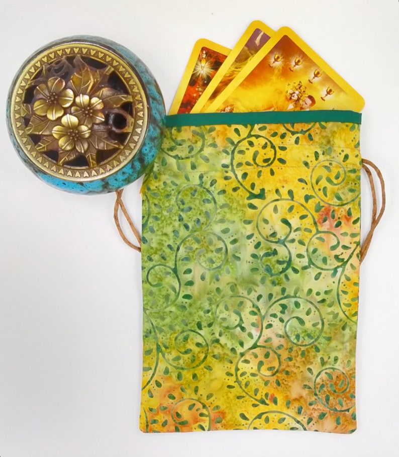 May include: A green and yellow fabric pouch with a drawstring closure. The pouch is decorated with a swirling floral pattern. The pouch is filled with tarot cards.