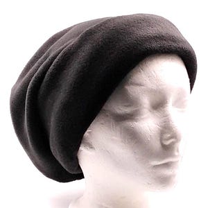 May include: A dark charcoal gray beanie hat made of soft fleece fabric. The hat features a wide, folded brim that encircles the head, with a slouchy, rounded crown that creates soft folds and gathers in the material for a relaxed fit.