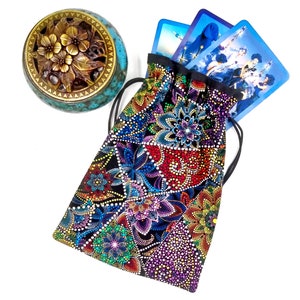 May include: A colorful drawstring bag with a mandala pattern, perfect for storing tarot cards. The bag is made of black fabric with a variety of colors, including red, blue, green, and purple. The bag is shown with a set of tarot cards inside.