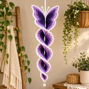 May include: A hanging crochet spiral ornament featuring a butterfly top in shades of deep purple and lavender with a white border. The structure consists of a long, twisting, multi-layered purple crochet coil that ends with a single white bead.
