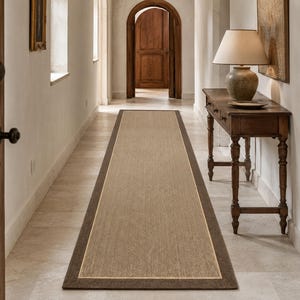Puede incluir: Una alfombra de pasillo larga y rectangular con un panel central de color tostado claro texturizado con un sutil patrón de espiga, enmarcado por un borde ancho de color marrón oscuro sólido que recorre todo el perímetro.