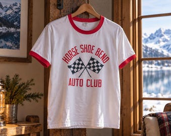 May include: A white ringer t-shirt with red trim on the collar and sleeve cuffs. The front features red text that reads HORSE SHOE BEND AUTO CLUB, centred above a graphic of two crossed black and white checkered racing flags.