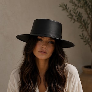 May include: A solid black hat with a flat crown and a wide, structured brim. The hat features a smooth, matte finish and a matching black band encircling the base of the crown, creating a clean, uniform appearance across the entire headwear piece.