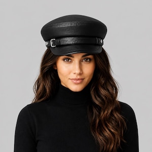 May include: A black leather baker boy cap featuring a structured crown, a short stiff brim, and a decorative horizontal leather strap across the front. The strap is secured with silver-toned metal hardware, including a small buckle and side studs.