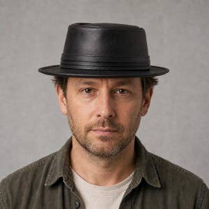 May include: A black fedora hat with a flat crown and a structured brim. The hat features a matching black band wrapped around the base of the crown, providing a clean and uniform appearance. The material has a smooth, matte finish throughout.