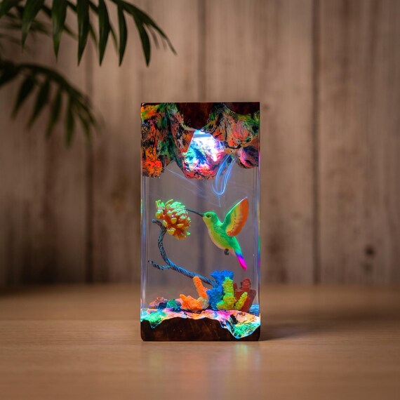 A hummingbird suspended in glowing amber epoxy resin fused with real wood — it's a tiny terrarium of light that doubles as a night lamp.