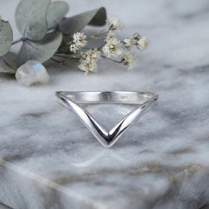 Könnte beinhalten: Ein silberner V-förmiger Ring mit einer glatten, polierten Oberfläche. Das innere Band des Rings ist deutlich mit dem Stempel 925 versehen, was auf eine Zusammensetzung aus Sterlingsilber hinweist. Der Ring hat ein spitzes Chevron-Design.
