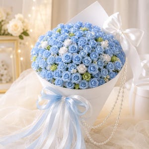 May include: A large bouquet of light blue roses with accents of white and pale green flowers, wrapped in white paper. The arrangement is decorated with a large white satin bow, a light blue ribbon, and a long strand of white faux pearls.