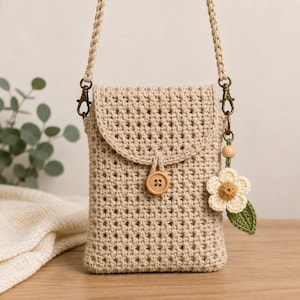 May include: A beige crochet crossbody bag featuring a textured stitch pattern, a flap closure secured with a single wooden button, and a braided strap. A small crocheted flower charm with a green leaf is attached to the brass-toned metal hardware.