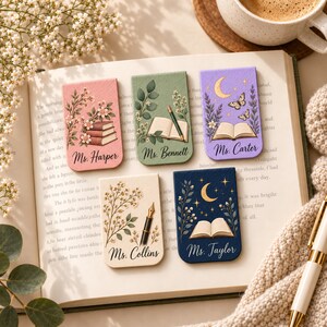 May include: Five rectangular magnetic bookmarks featuring personalized names and illustrations. Designs include stacked books, open books with pens, and celestial motifs with moons, stars, and butterflies in pink, green, lavender, cream, and navy blue colors.