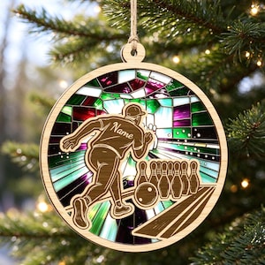 May include: A round wooden ornament featuring a laser-cut bowling scene with a person throwing a ball toward pins. The background displays a colorful stained-glass pattern in shades of green, purple, and white. The word Name is engraved on the shirt.