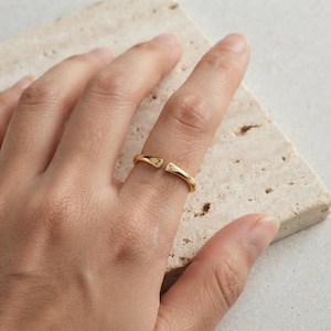 Puede incluir: Un anillo abierto de tono dorado con dos extremos, uno grabado con la letra Z y el otro con la letra S. La banda tiene un acabado liso y pulido, diseñada para ser ajustable, con los dos extremos separados por un pequeño espacio.
