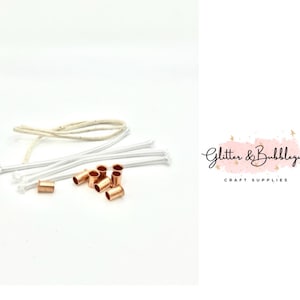 May include: Candle-making supplies on a white background. The image shows several white wicks, a beige wick, and copper-colored wick holders. The text "Glitter & Bubblegum CRAFT SUPPLIES" is in the background.