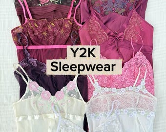 Pode incluir: Uma coleção de camisetes e camisolas em várias cores, incluindo bordô, rosa e branco, com acabamentos em renda, bordados florais e alças finas. A imagem inclui um texto central que diz Y2K Sleepwear.