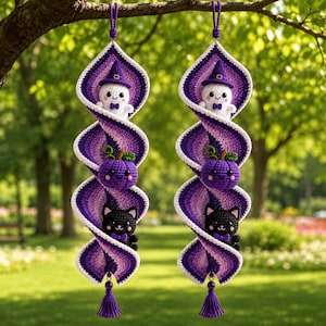 May include: Two identical hanging spiral decorations made of crocheted yarn in shades of purple and white. Each spiral features three small stuffed figures: a white ghost wearing a purple witch hat, a purple pumpkin, and a black cat with a bow.
