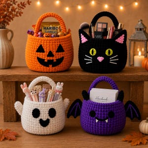 Puede incluir: Cuatro cestas de ganchillo con diseños de Halloween: una calabaza naranja, un gato negro con orejas rosas, un fantasma blanco con bolígrafos de animales y un murciélago morado con alas que sostiene una tarjeta que dice Handmade with love.