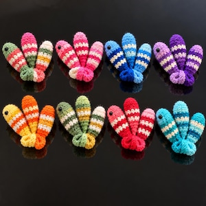 May include: Eight sets of three small, crocheted fish-shaped toys arranged in two rows. Each fish features horizontal stripes in various color combinations, including pink, green, yellow, blue, purple, and red, with a single black bead eye.