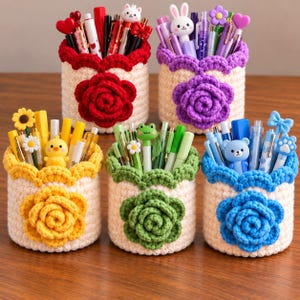 May include: Five cylindrical crochet pen holders in cream with scalloped rims and large floral appliques in red, purple, yellow, green, and blue. Each holder is filled with various pens and pencils featuring decorative toppers like animals and flowers.