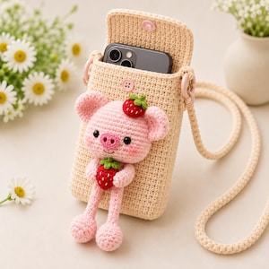 May include: A beige crochet crossbody phone bag featuring a three-dimensional pink piglet character holding a red strawberry. The piglet has a matching strawberry on its head. The bag includes a long matching strap and a snap button closure.