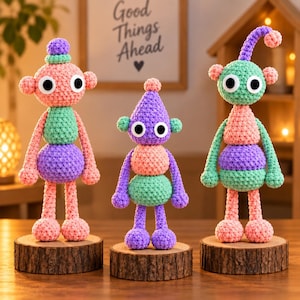 May include: Three handmade crochet dolls with large white and black plastic eyes, each standing on a circular wooden base. The dolls feature colorful yarn segments in pink, mint green, and purple, with varied shapes including round heads and pointed tops.