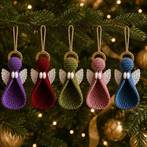 May include: Five crocheted angel ornaments hanging in a row, each featuring a round head, a flared body, and white wings. The angels are colored purple, dark red, olive green, dusty pink, and blue, with each topped by a gold halo and a hanging loop.