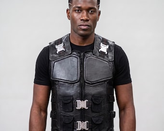 May include: A black leather tactical vest featuring a central zipper closure, two large chest panels, and four smaller front pockets. The vest is secured with silver-toned metal quick-release buckles on the chest and shoulder straps.