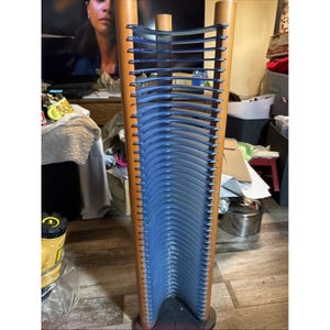 May include: A vertical media storage rack featuring two light brown wooden side supports connected by a series of thin, curved, blue plastic dividers designed to hold individual discs in a stacked, upright arrangement.