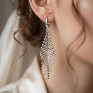 May include: A silver-toned dangle earring featuring a diamond-shaped mesh design composed of small, interconnected metallic beads. The earring hangs from a simple circular hoop closure that secures through the earlobe, creating a long, slender silhouette.