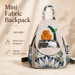 May include: A mini fabric backpack measuring approximately 30 x 20 x 10 cm. The bag features a beige linen-like upper section with an embroidered orange armchair, a green plant, and a white cat. The lower portion has a blue, yellow, and white floral pattern.