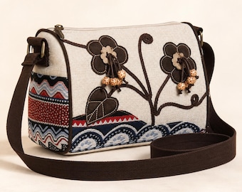May include: A beige fabric shoulder bag featuring dark brown floral appliqués with dangling wooden beads. The lower section displays a multi-colored woven pattern with red, blue, and white zigzag and scalloped motifs. It includes a dark brown strap.