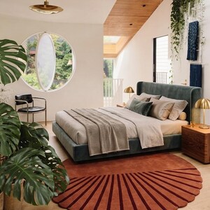 May include: A bedroom featuring a dark green upholstered bed with light gray bedding and a textured throw blanket. A large, semi-circular, rust-colored rug with radiating dark red lines sits on the light wood floor beneath the bed frame.