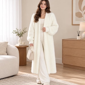 Peut inclure: Un long cardigan ouvert et duveteux de couleur crème à manches longues, associé à un débardeur et un pantalon large assortis de couleur crème. Un petit sac à main structuré de couleur crème avec une anse est tenu à la main.