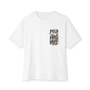 May include: A white short-sleeve t-shirt featuring a graphic on the left chest area. The graphic includes the dark blue text PULP PRESS PULL stacked vertically, accompanied by illustrations of a printing press and paper sheets in brown tones.