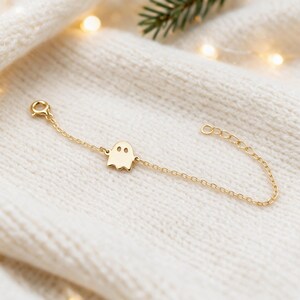 Op de afbeelding: Een goudkleurige armband met een fijne ketting en een platte, spookvormige bedel in het midden met twee kleine ronde uitsparingen als ogen. De armband is voorzien van een kleine ronde sluiting aan het ene uiteinde en een verstelbare schakelketting.