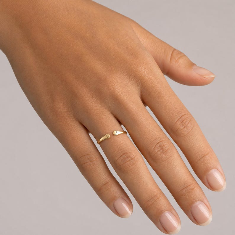 May include: A gold-toned open ring featuring two small, flat, rounded ends. Each end is engraved with a single uppercase letter, specifically the letter S on one side and the letter Z on the other, creating a personalised and adjustable band design.