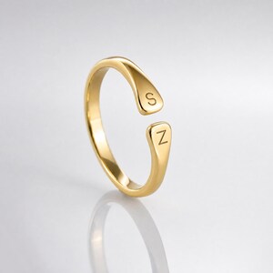 May include: A gold-toned open ring featuring a smooth, polished finish. The two ends of the band are slightly flattened and rounded, with the letter S engraved on the top terminal and the letter Z engraved on the bottom terminal of the opening.