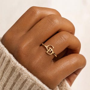 May include: A gold ring featuring a polished finish with two interlocking letters, C and P, centered on the thin band. The metal has a warm, reflective tone, and the design consists of a capital C positioned above a capital P in a serif font.