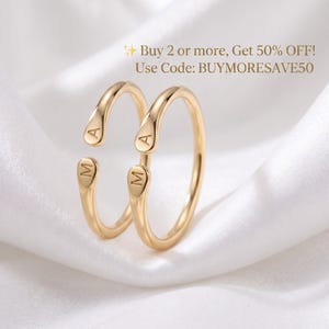 May include: Two gold-toned open rings featuring rounded ends, each engraved with the letters A and M. The text Buy 2 or more, Get 50% OFF! Use Code: BUYMORESAVE50 is visible above the rings. The rings have a smooth, polished finish.