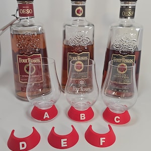 May include: Three glass bottles of Four Roses bourbon with dark caps and embossed rose designs, accompanied by three clear tasting glasses with red silicone bases labelled A, B, and C, and three additional red silicone bases labelled D, E, and F.