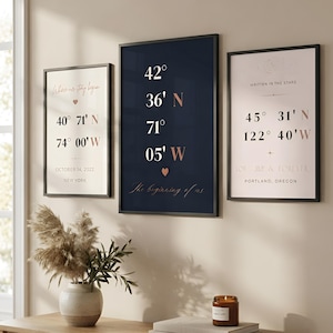 May include: Three framed wall art prints featuring geographic coordinates and text. The left print displays New York coordinates, the center navy print shows coordinates with a heart, and the right print features Portland, Oregon details.